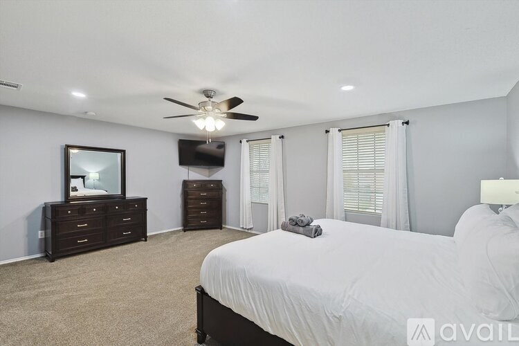 A bedroom with a large bed, a dresser, and a ceiling fan.