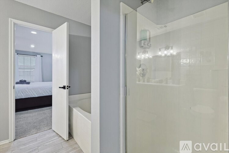A bedroom with a glass shower door and a white door leading to a bedroom.