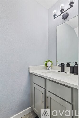 A bathroom with a white sink and grey cabinets.