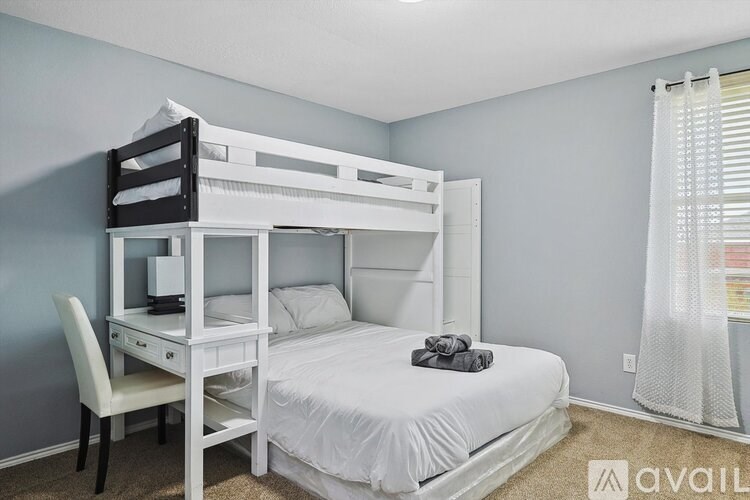 A white bunk bed with a desk underneath and a chair beside it in a room.