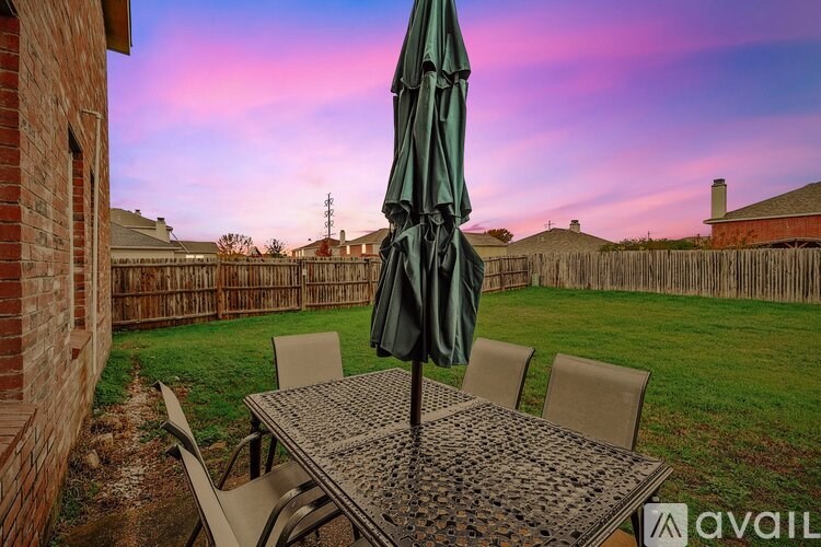 A patio table with chairs and an umbrella is set up in a backyard.