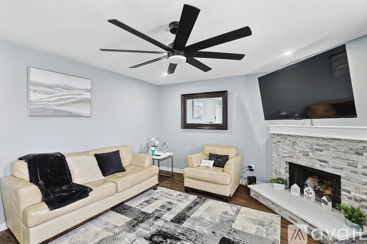 A living room with a beige couch, a chair, a fireplace, and a ceiling fan.