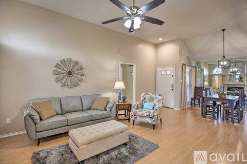 A living room with a grey couch, a white chair, and a ceiling fan.