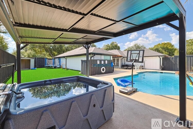A hot tub is in the middle of a backyard with a basketball hoop and a pool.
