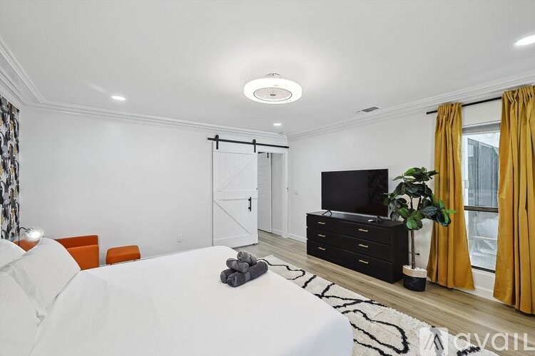 A modern bedroom with a white bed, orange pillows, a black dresser, and a television.