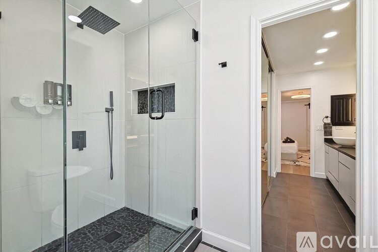 A modern bathroom with a walk-in shower and a view into another room.