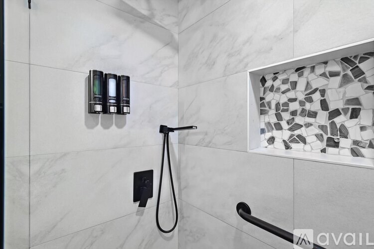 A shower area with a black shower head and a black handle.