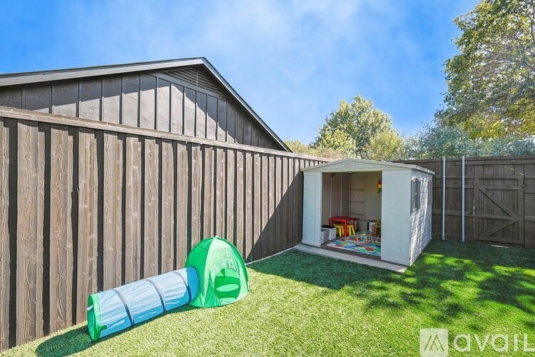 A backyard with a wooden fence, a playhouse, and a slide.