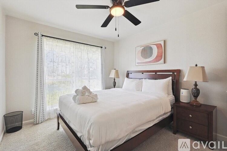A bedroom with a bed, nightstand, and window with curtains.