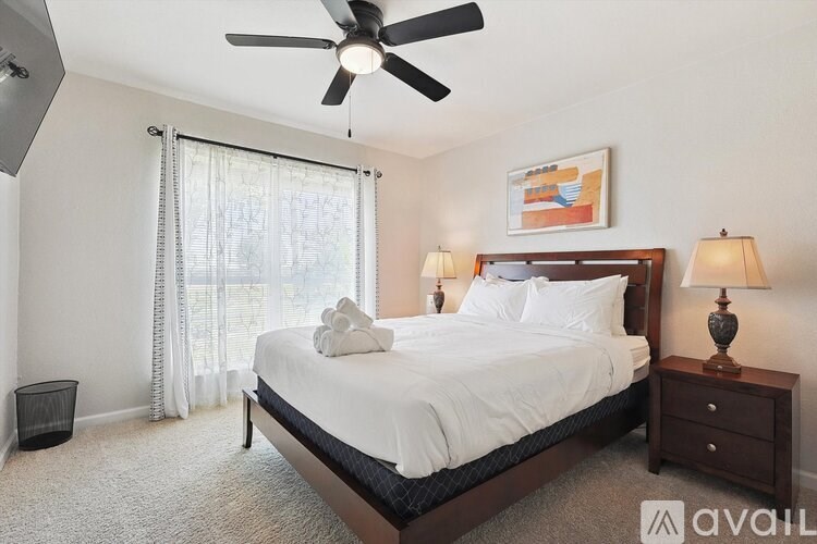A bedroom with a large bed, a ceiling fan, and a window with curtains.
