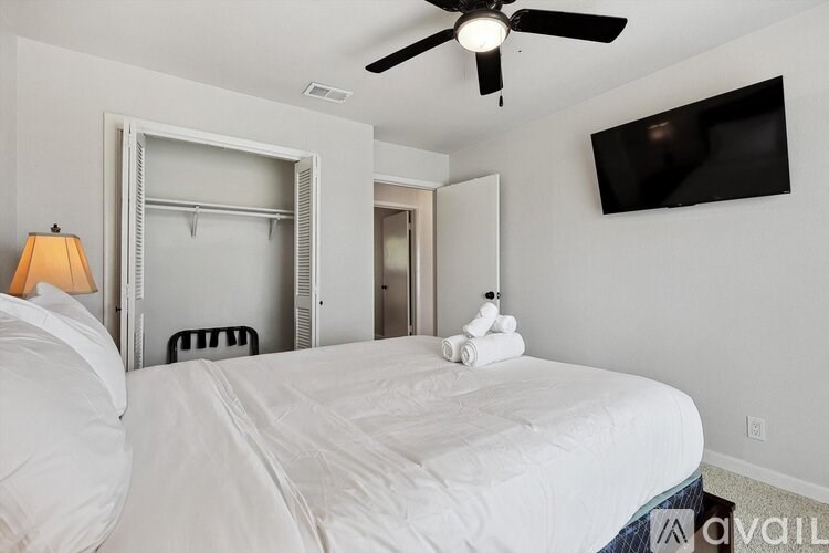 A bedroom with a large bed, a ceiling fan, and a flat-screen TV mounted on the wall.