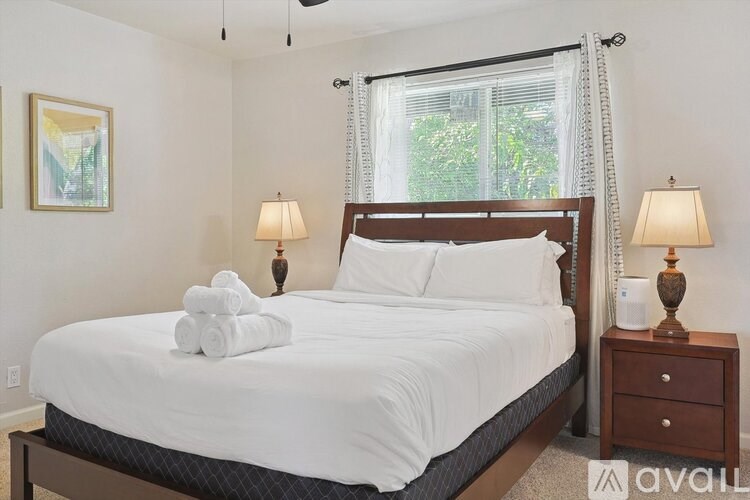A bedroom with a large bed, two lamps, and a painting on the wall.