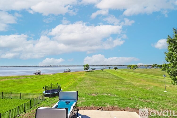 A view of a field with a trampoline and a body of water in the distance.