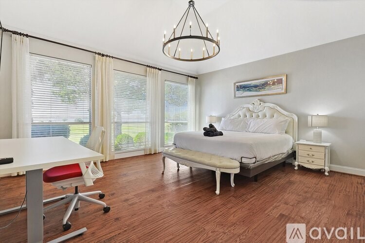 A bedroom with a large bed, a desk with a chair, and a chandelier.