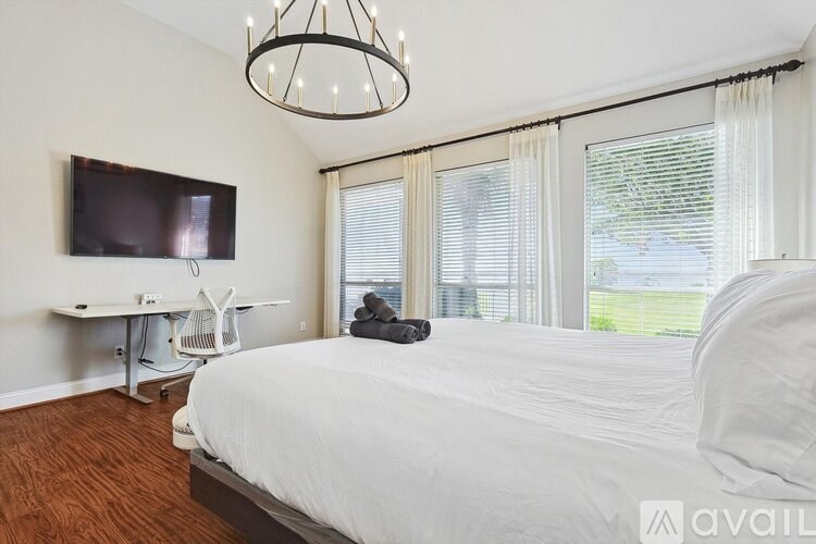 A bedroom with a large bed, a desk with a chair, and a television mounted on the wall.