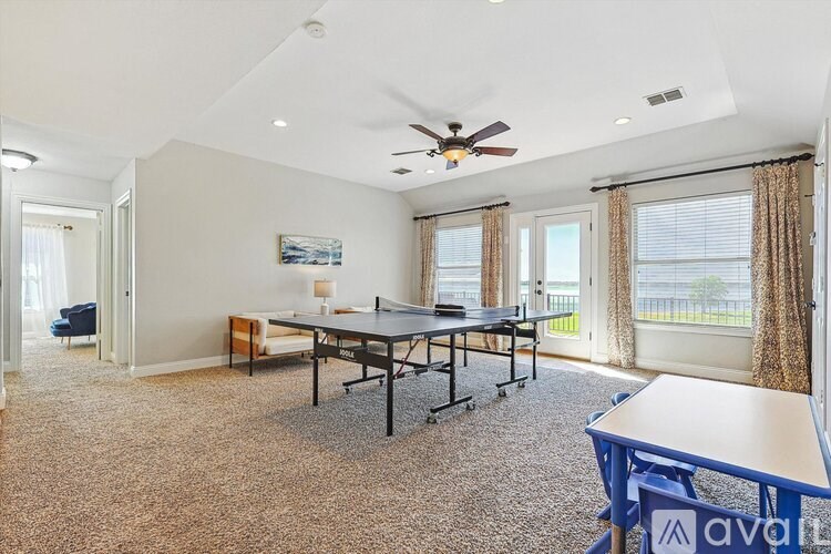 A spacious room with a table and chairs, a ceiling fan, and a view of the outdoors through the windows.