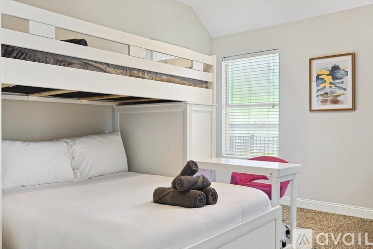 A white bed with a white pillow and a white bedside table with a red cushion and a picture on the wall.