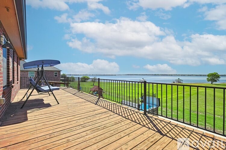 A wooden deck with a black railing overlooking a grassy area.