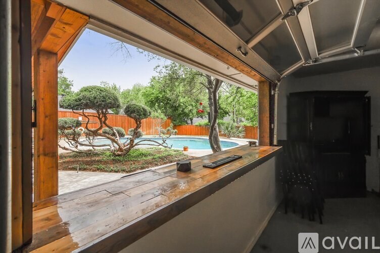 A room with a view of a pool and trees through a window.