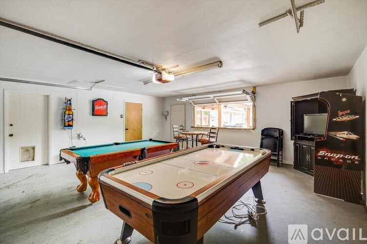 A pool table is in the middle of a room with a TV and a bar.