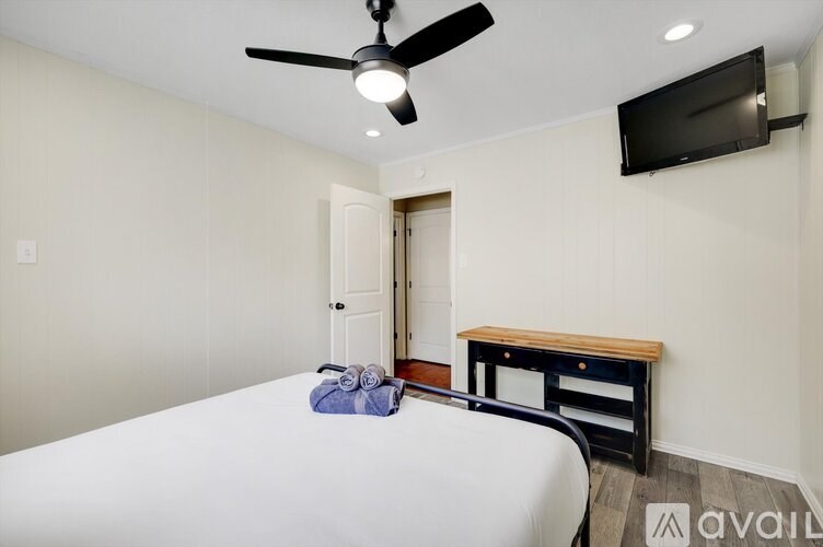 A bedroom with a bed, a ceiling fan, and a TV mounted on the wall.