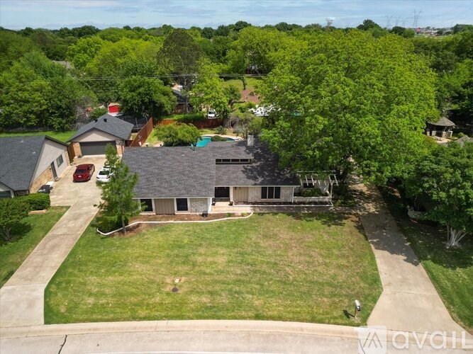 A house with a grey roof is surrounded by a green lawn and trees.