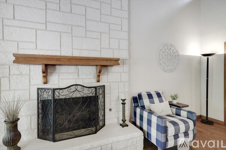 A black fireplace with a wooden mantle and a blue and white checkered chair in front of it.