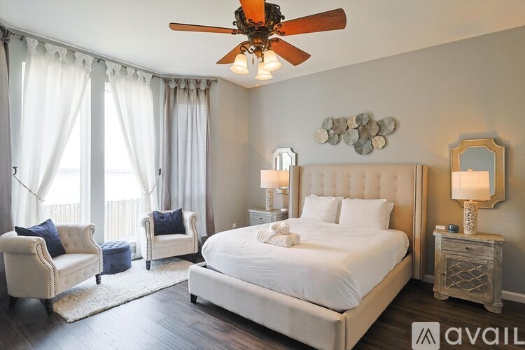 A bedroom with a large bed, two chairs, and a ceiling fan.