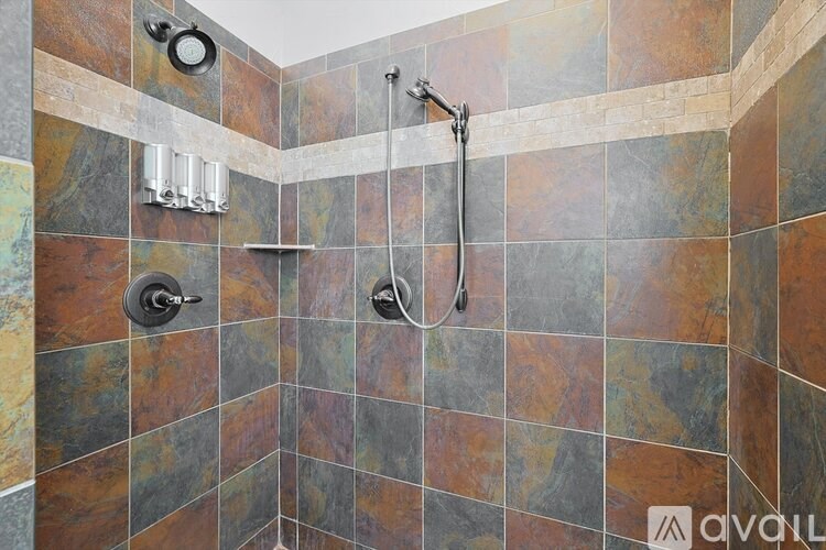 A shower area with a tile wall and a hand held shower head.