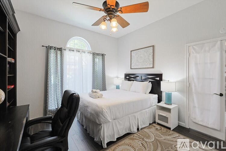 A bedroom with a bed, chair, and ceiling fan.