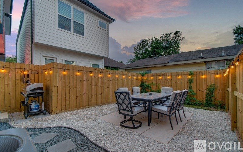 A backyard with a patio table and chairs, a fire pit, and string lights.