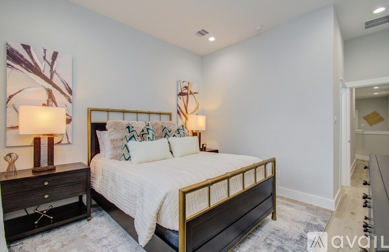 A bedroom with a large bed, a nightstand with a lamp, and a painting on the wall.