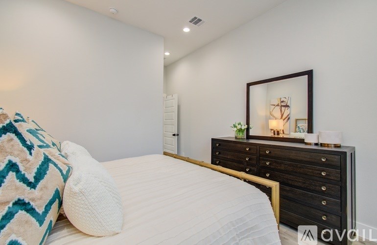 A bedroom with a white bed, a black dresser, and a framed picture on the wall.