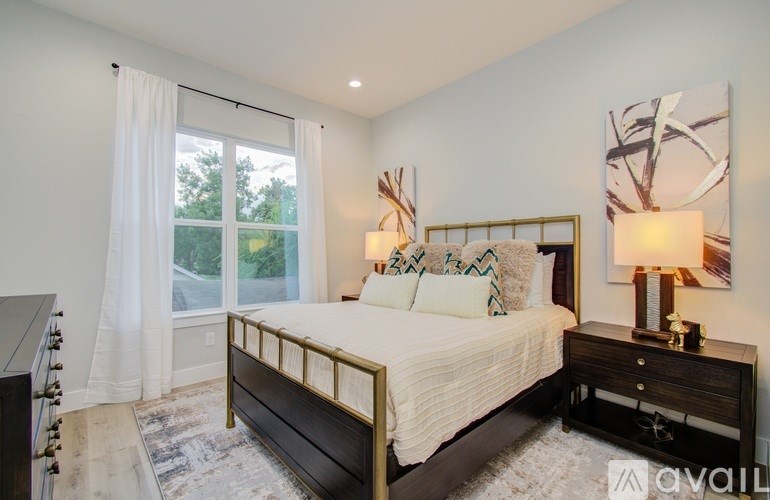 A bedroom with a large bed and a window with white curtains.