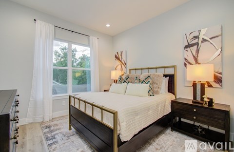 A bedroom with a large bed and a window with white curtains.
