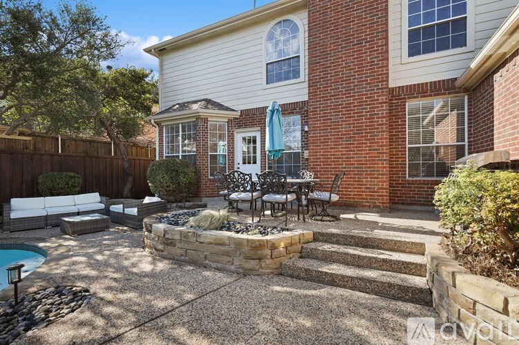 A backyard with a patio, a pool, and a brick house.