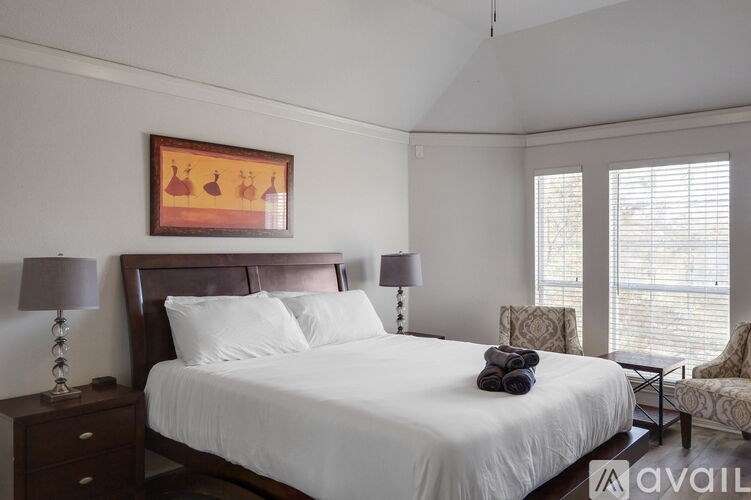 A bedroom with a large bed, two lamps, and a painting on the wall.