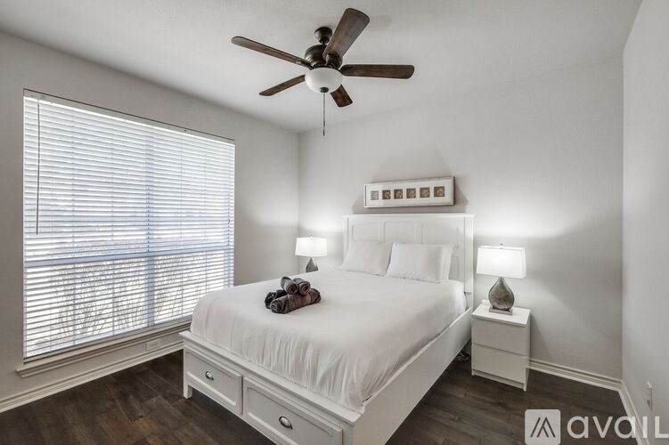 A bedroom with a large bed, a ceiling fan, and a window with blinds.