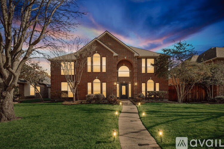 A large house with a brick facade and arched windows is lit up at dusk.