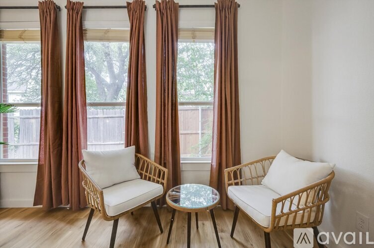 Two chairs and a table are in front of a window with brown curtains.