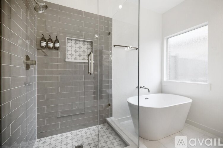 A modern bathroom with a white bathtub and grey tiled walls.