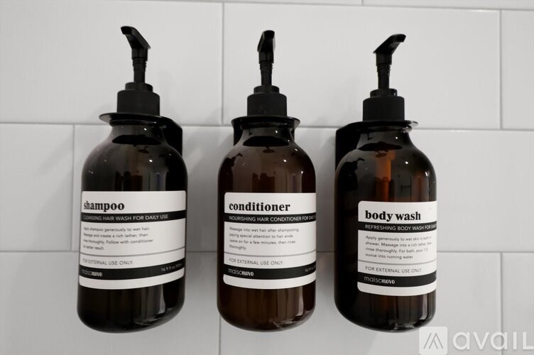Three bottles of shampoo, conditioner and body wash are lined up on a tiled wall.