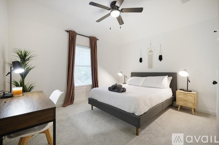 A bedroom with a large bed, a ceiling fan, and a desk with a lamp.