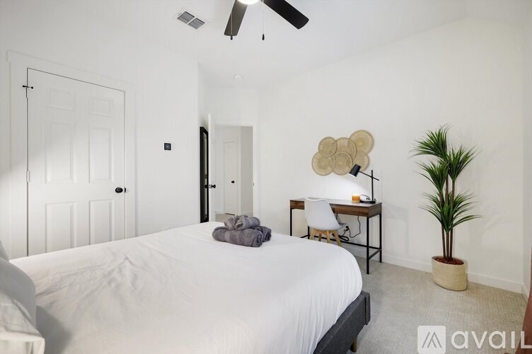 A bedroom with a bed, desk, chair, and plant.