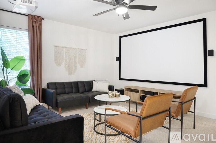 A living room with a black couch, a white screen, and a ceiling fan.