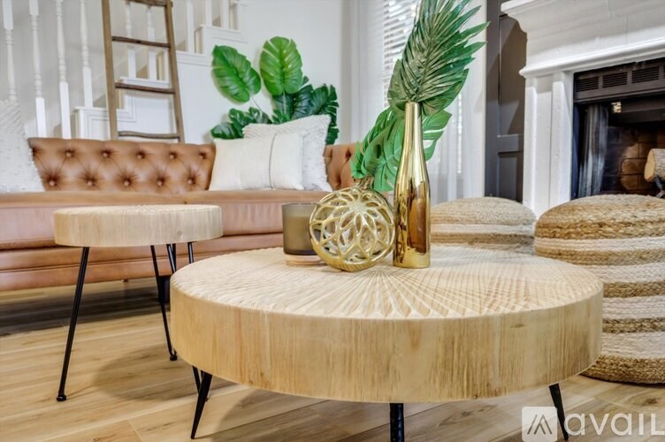 A round wooden table with a decorative vase on top sits in a room with a brown sofa and a fireplace.
