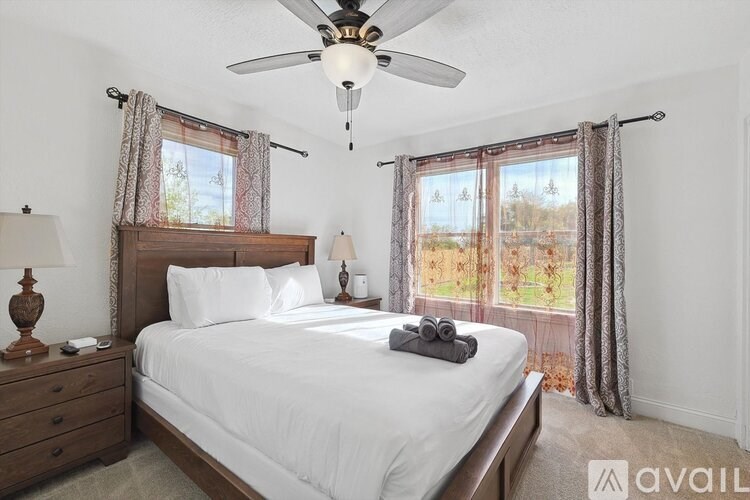 A bedroom with a large bed, a ceiling fan, and a window with curtains.