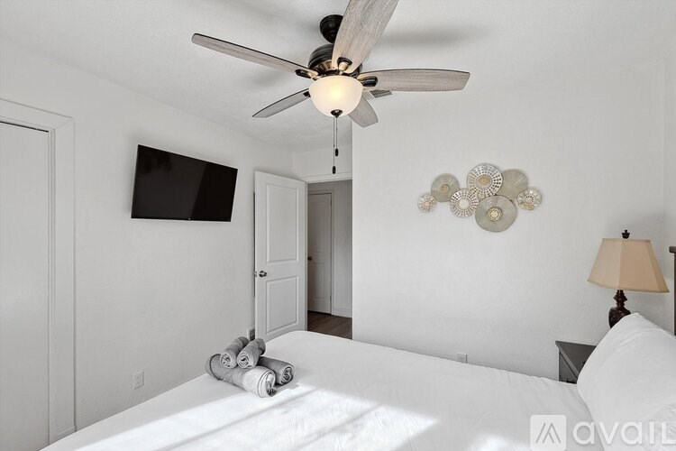 A bedroom with a bed, a ceiling fan, and a wall-mounted television.