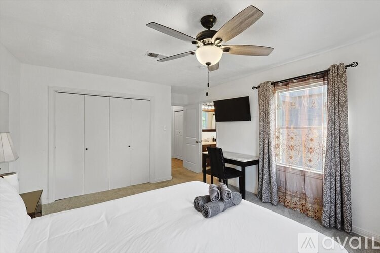 A bedroom with a bed, a ceiling fan, and a window with curtains.