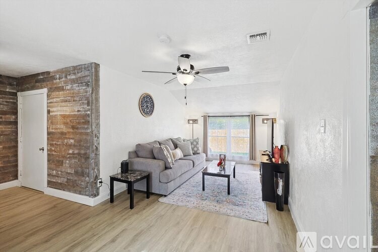 A living room with a grey couch, a ceiling fan, and a wooden accent wall.